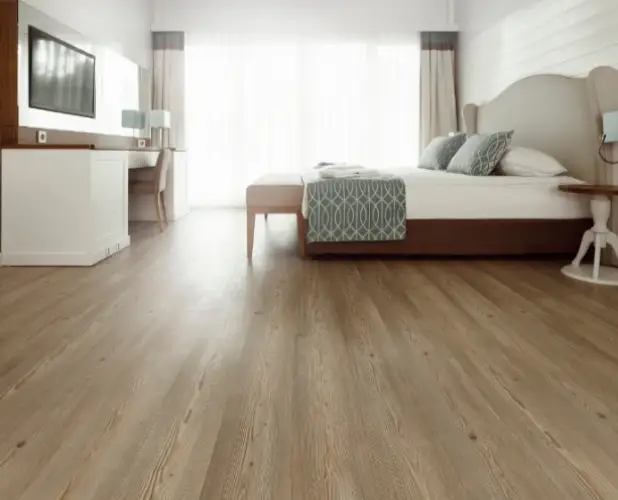 Elegant bedroom with hardwood flooring in Brampton, stylish bed with blue accents, desk, TV, and bright windows, by Best Tiles and Flooring.